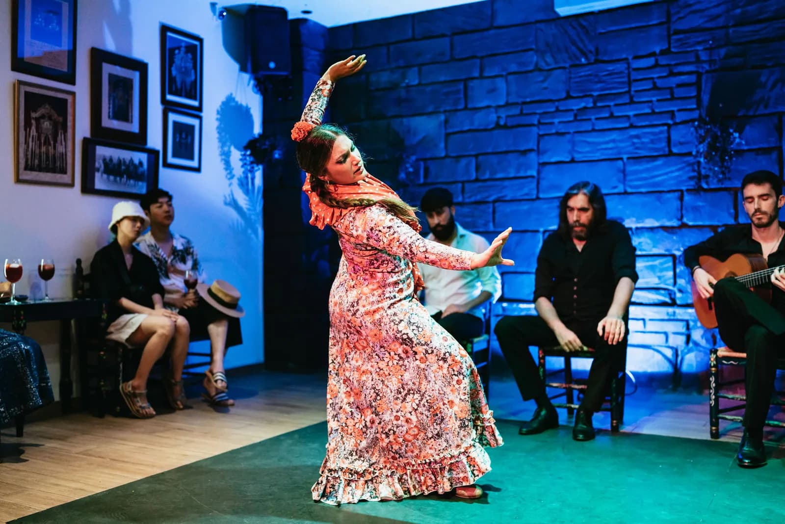 Bailaora con vestido floreado en pleno giro sobre el escenario intimo de Baraka Sala Flamenca, con guitarrista y cantaor detras.