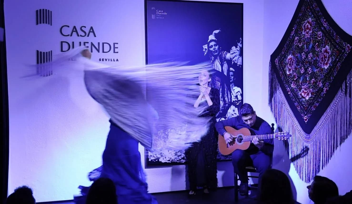 Bailaora con manton transparente en movimiento sobre el escenario de Casa Duende, con guitarrista y el rotulo del local al fondo.