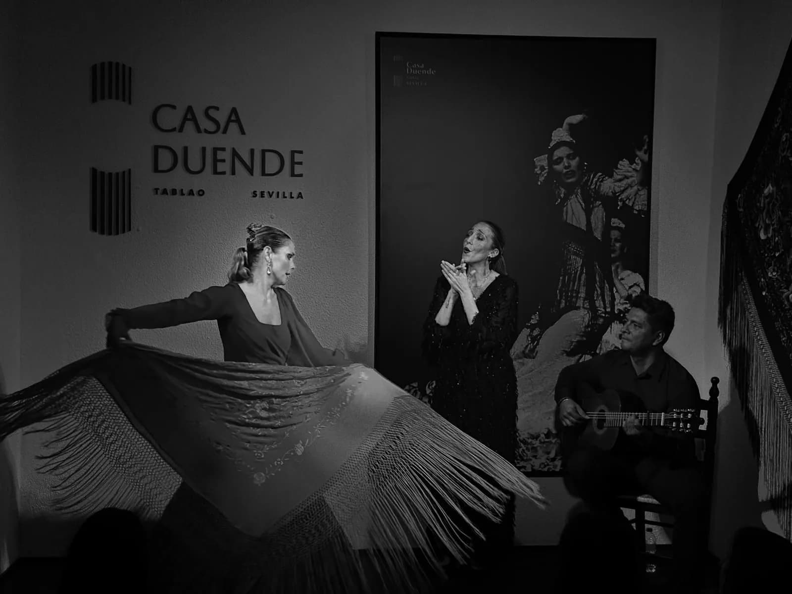 Bailaora con bata de cola negra actuando junto a un guitarrista en el escenario de Casa Duende, fotografia en blanco y negro.