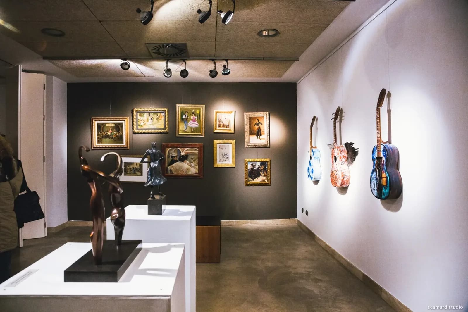 Sala de exposiciones del Museo del Baile Flamenco con esculturas, guitarras y fotografias en las paredes.