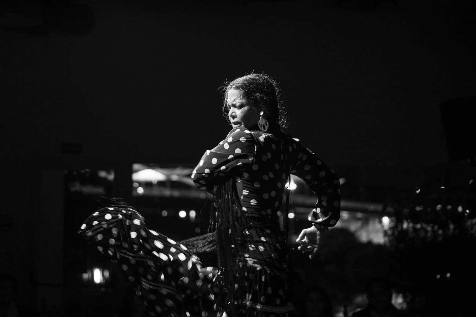 Bailaora con vestido de lunares bailando con el perfil de Sevilla iluminado al fondo, fotografia en blanco y negro.