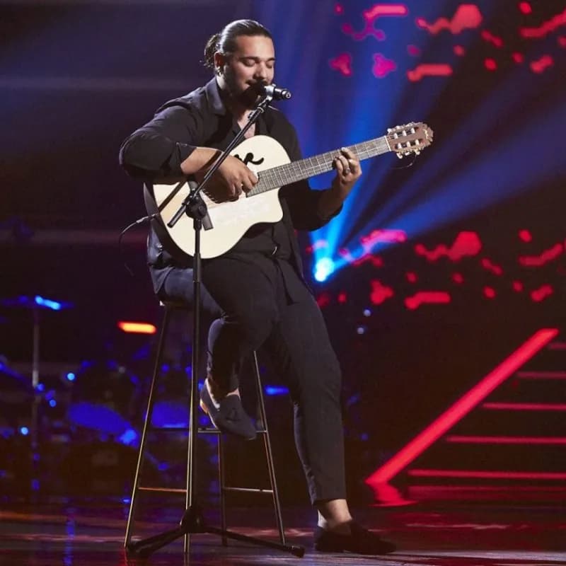 Guitarrista cantando y tocando de pie sobre el escenario de La Cantaora con iluminacion azul y roja.
