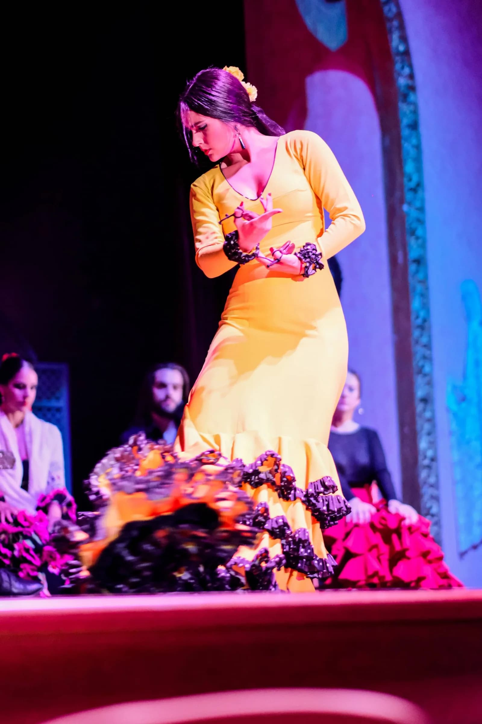 Bailaora con vestido amarillo de volantes posando sobre el escenario iluminado en azul de El Palacio Andaluz.